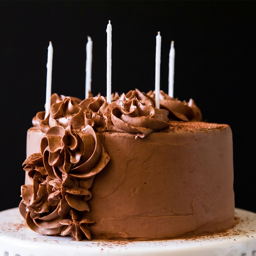 Chocolate Buttercream Ingredients A dark chocolate cake with lit birthday candles showing the rich color of the chocolate frosting.