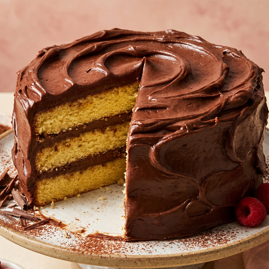 Chocolate Sour Cream Frosted Cake A beautiful yellow layer cake covered in thick, dark chocolate sour cream frosting on a white plate.