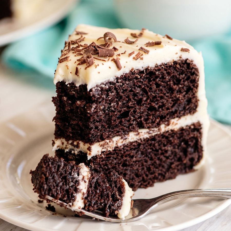 A slice of chocolate velvet cake with cream cheese icing on a plate with a fork