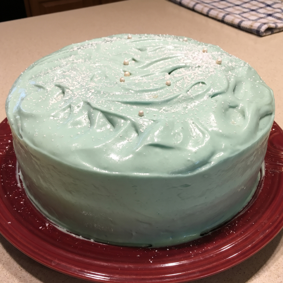 Round cake topped with glossy seafoam frosting on a red plate