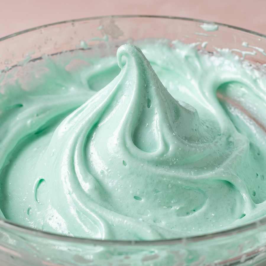 Whipped seafoam frosting being made in a mixing bowl over a double boiler