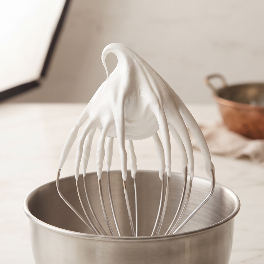 Glossy Stiff Peaks of 7 Minute Frosting A wire whisk coated in thick, glossy white 7-minute frosting with dramatic peaks.