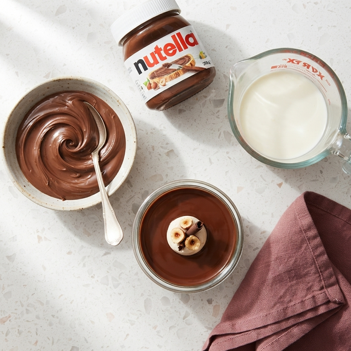 Two Ingredient Ganache An overhead shot of a jar of Nutella and a small glass jug of heavy cream on a marble surface.